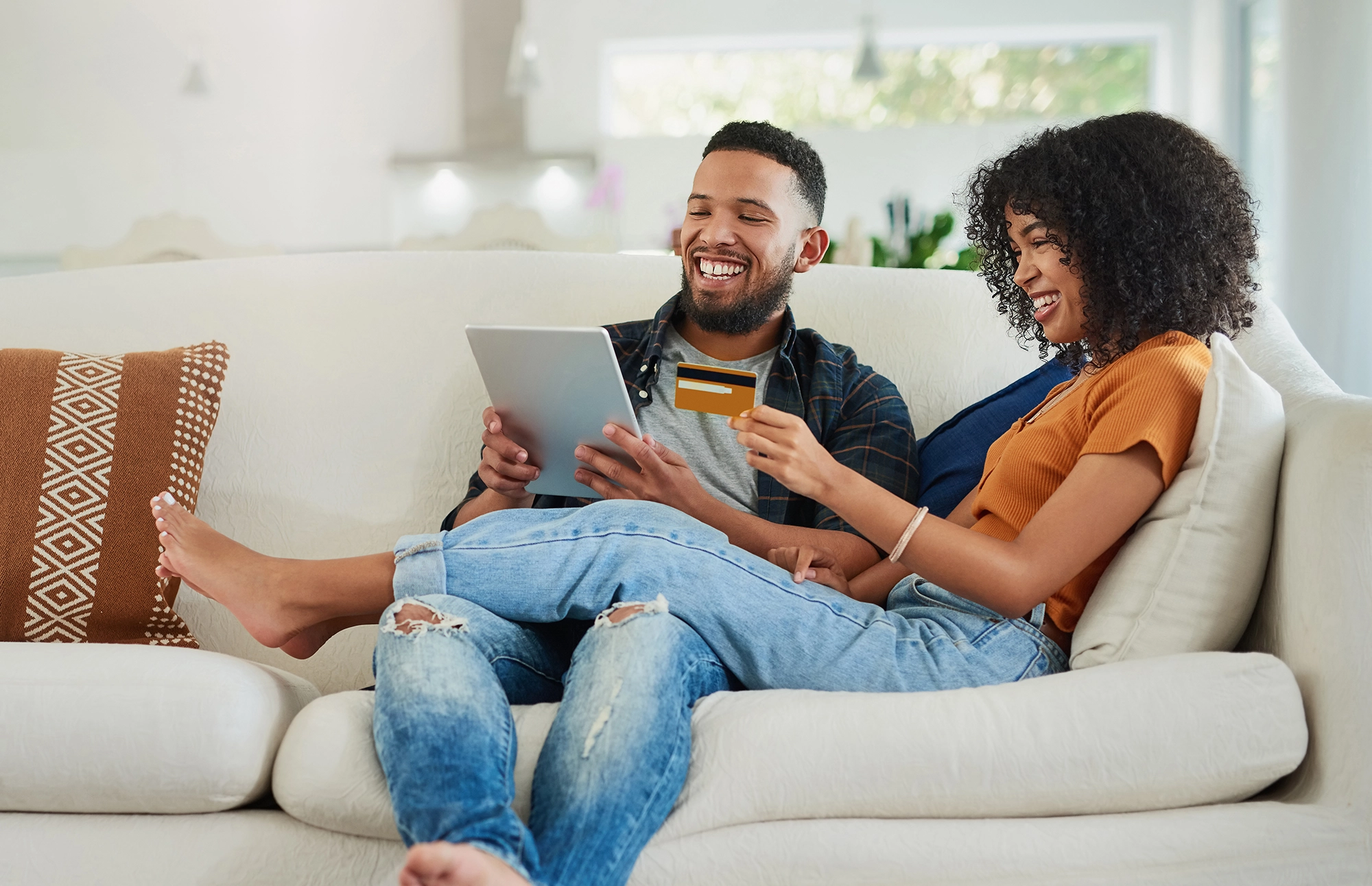 Couple smiles as they enter in a card number into a tablet while sitting on the couch